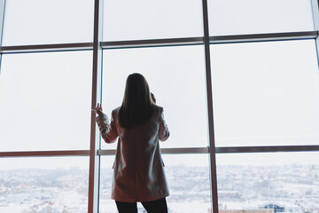 Successful business woman standing looking out the window enjoying the city view, confident wealthy...