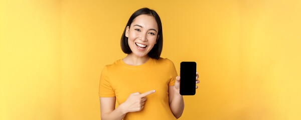 Beautiful happy asian girl showing mobile phone screen, application on smartphone gadget, standing...