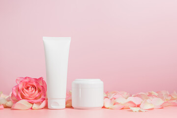 Face cream unbranded tube and cream bottle mockup with rose flower and petals on pink background, copy space, face skin care containers for natural cosmetic design and branding