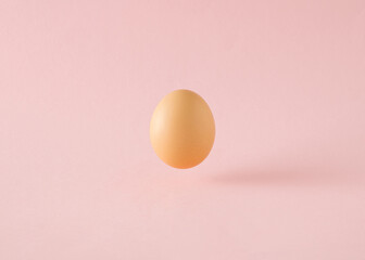 An egg levitates above a pink background and its shadow. Minimalist Easter concept
