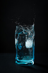 Ice falls into the glass. splash of frozen water. Blue beautiful wine glass