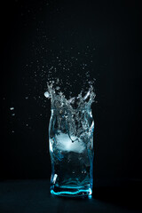 Ice falls into the glass. splash of frozen water. Blue beautiful wine glass