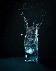 Ice falls into the glass. splash of frozen water. Blue beautiful wine glass