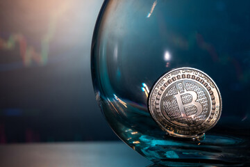 Close-up of a silver Bitcoin on a blue reflective surface in a glass and the histogram of currency in the background