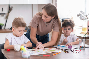 A loving young mother and small children preschool sons sit at the kitchen table together making paper applications,homework and teaching children