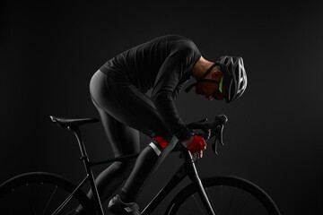 male cyclist riding road bicycle on black background - obrazy, fototapety, plakaty