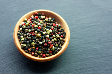 peppercorns, black pepper, white, green, red pepper, aromatic seasoning, spices, cooking ingredients, top view, in a wooden bowl on a black background, space for text 