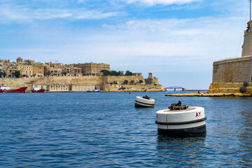 Fototapeta na wymiar The Grand Harbour in Malta with the tip of Fort St. Angelo and the City of Valletta with the Lower Barrakka Gardens, Pixkerija and Siege Bell Memorial.