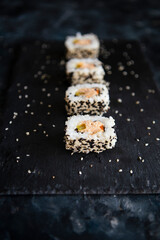 Japanese sushi food rolls served on blackboard plate, dark background