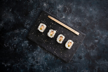 Japanese sushi food rolls served on blackboard plate, dark background - top view