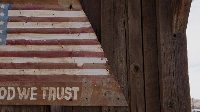 This panning video shows an old metal sign with an American flag painted on it, hanging on a wooden wall.