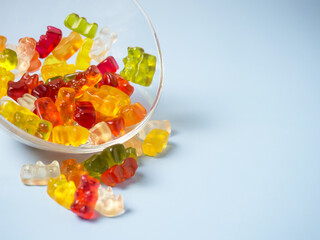 Bowl with tasty bright gummy bears on blue table