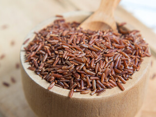 Red rice (brown rice) in a wooden bowl, red rice scattered on the ground.close up