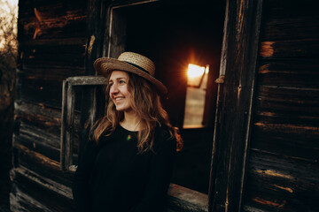 beautiful Ukrainian girl in black clothes and a straw hat stands near the old wooden house. The war...
