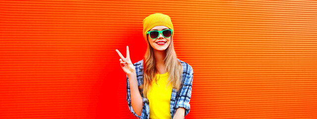 Portrait of happy smiling young woman wearing colorful clothes, yellow hat on orange background