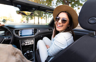 Joyful young woman sitting on convertible car smiling at camera - Happy couple driving on the road...