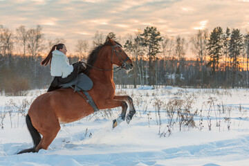 A girl in a white cloak rides a brown horse in winter.