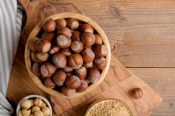 Whole raw hazelnut in a wooden bowl with peeled hazelnuts and nut flour on textured wooden background, top view, close up. Paleo and ketogenic diet baking cooking concept, gluten free food