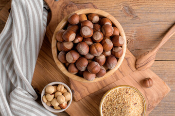 Whole raw hazelnut in a wooden bowl with peeled hazelnuts and nut flour on textured wooden background, top view, close up. Paleo and ketogenic diet baking cooking concept, gluten free food