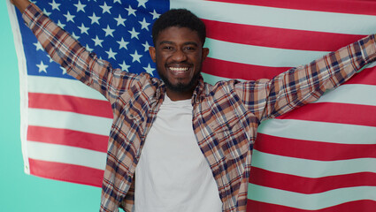 Portrait of african american man in shirt waving, wrapping in American USA flag, celebrating, human rights, freedoms. Independence day. Adult guy indoors studio shot isolated alone on gray background