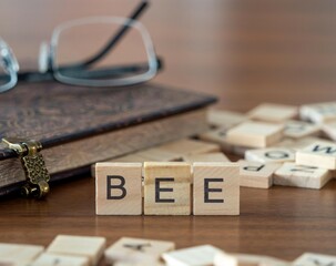 bee word or concept represented by wooden letter tiles on a wooden table with glasses and a book