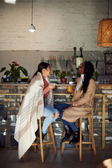 Two multicultural friends sit in the cafeteria, drink beverages, and chat.