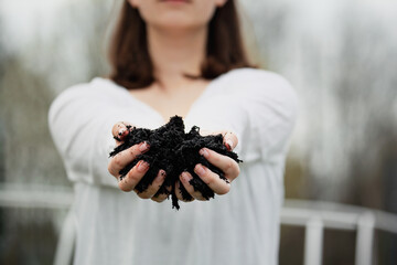 Young woman in front of a garden with her hands outstretched holding fresh compost for Earth Day....