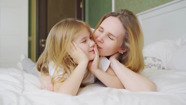 mom and daughter in bed having fun, kissing and hugging.