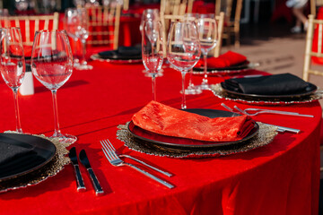 Guests table setting for banquet in black, red and gold style. Elegant and luxury dinner arrangement: decor, tablecloth, plates, glasses, napkins, cutlery. Themed birthday or wedding party celebration