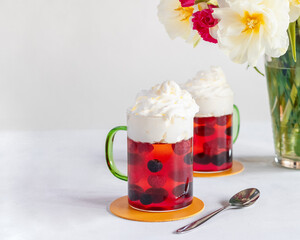 Colorful fruit jellies with whipped cream in decorative cups. Blueberries, raspberries. Bouquet of flowers in the background. Background for a culinary blog.