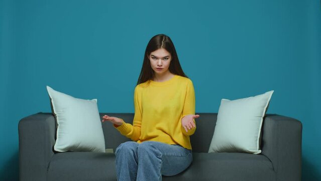 Funny young girl showing stupid gesture with fingers near temples, blaming somebody in crazy dumb plan, sitting on couch