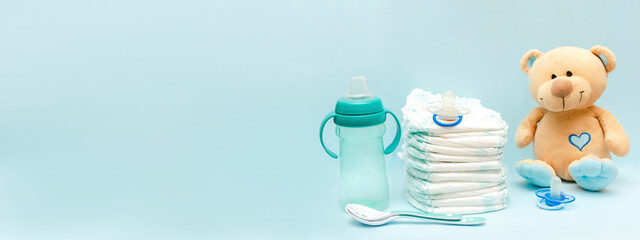 Stack of diapers with cute teddy bear toy, bottle milk, pacifier on table. set for infant newborn...