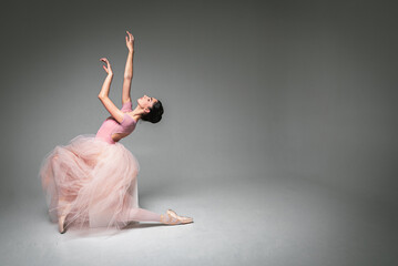 young pretty, fragile, beautiful ballerina dancing in a long pale pink dress with a tulle on a uniform background, hand movements, restrained tone. Ballet, dance, dancer. Place for inscription - obrazy, fototapety, plakaty
