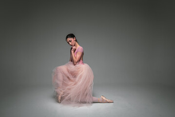 Fototapeta premium young pretty, fragile, beautiful ballerina dancing in a long pale pink dress with a tulle on a uniform background, hand movements, restrained tone. Ballet, dance, dancer. Place for inscription