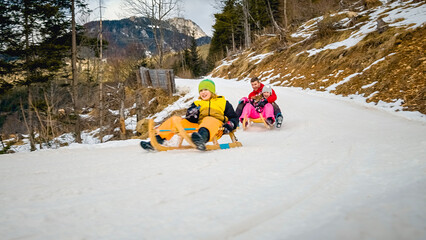 Happy Caucasian family, father, and two children sliding on wooden sleds along a snowy mountain...