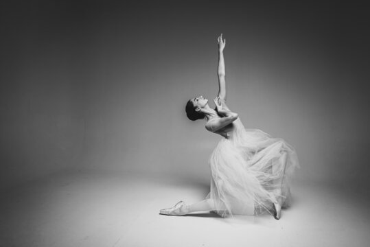 black-and-white photo, young pretty, fragile, beautiful ballerina dancing in a long pale pink dress with tulle on a uniform background, hand movements, restrained tone. Ballet, dance, dancer. Place fo