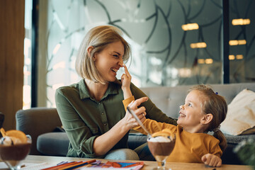 Playful mother and daughter have fun while eating mousse at home.
