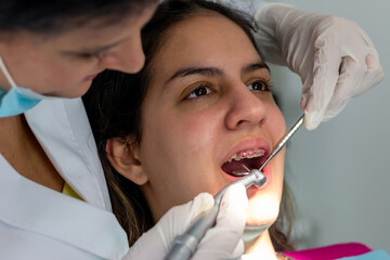 At the dental clinic. Teenager girl with braces, sitting on dentist chair with mouth opened while dentist is working on her ill tooth.