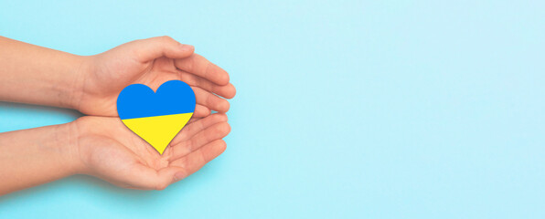 Hand holding a heart with Ukrainian national colors. Help Ukraine during the war