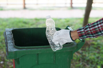 Hand wears glove, holds plastic bottle to throw into the bin in the park. Concept: recycling garbage sorting rubbish. Recycle plastic garbage. Waste management.     