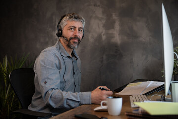 portrait d'un employé de bureau souriant qui communique avec un micro casque et un ordinateur dans son bureau. Il travaille à la maison à distance grâce à internet.