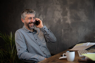 employé de bureau, homme d'affaire de 50 ans souriant qui discute au téléphone dans son bureau....