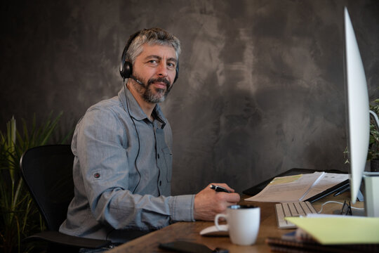 portrait d'un employ&eacute; de bureau souriant qui communique avec un micro casque et un ordinateur dans son bureau. Il travaille &agrave; la maison &agrave; distance gr&acirc;ce &agrave; internet.