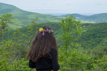 A young woman with long dark hair looks at the mountains, she has a wreath on her head. Caucasus Mountains