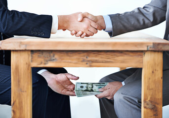 Under-the-table transactions.... Cropped shot of two businessmen shaking hands while money passes...