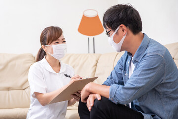 問診票に記入する看護師と患者（マスク）