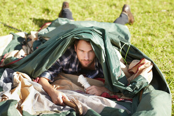 Hes clearly an amateur camper. Frustrated young man struggling to erect a tent outdoors.
