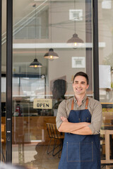 A young man stands in front of a storefront with an open sign behind the concept of opening a food and beverage outlet.