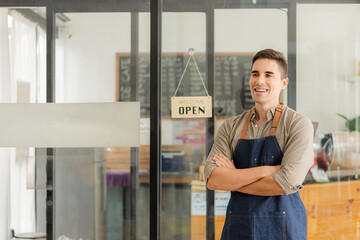 A young man stands in front of a storefront with an open sign behind the concept of opening a food and beverage outlet.