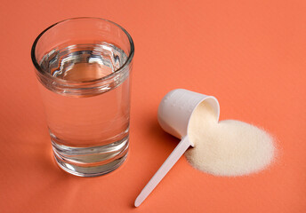 Powdered collagen protein in the spoon. Glass of water